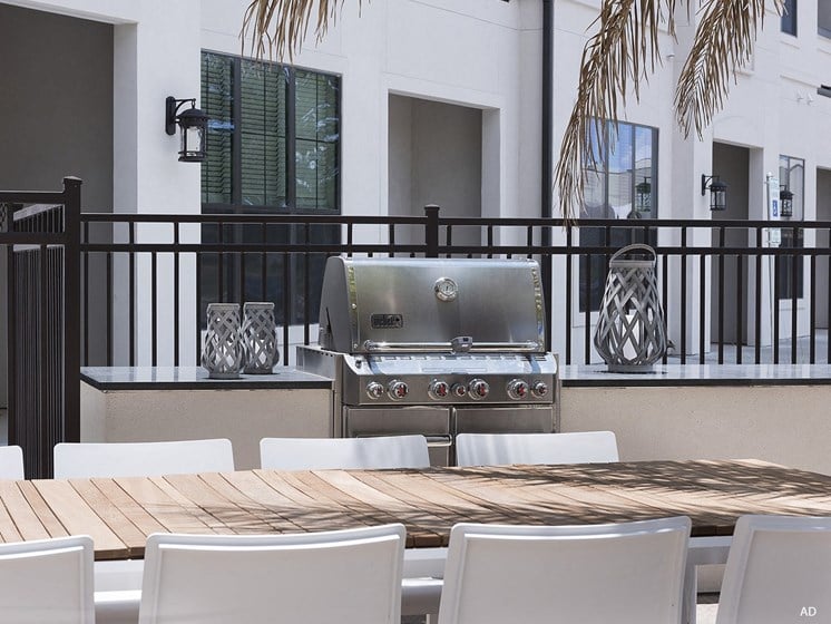a barbecue grill on a patio with white chairs and a wooden table